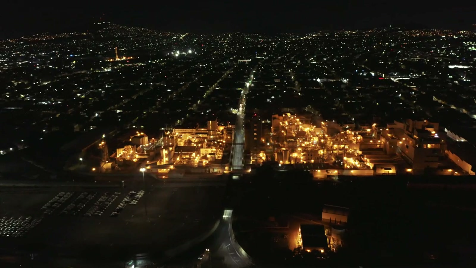 Night aerial of an illuminated industrial plant glowing against a dark city grid.