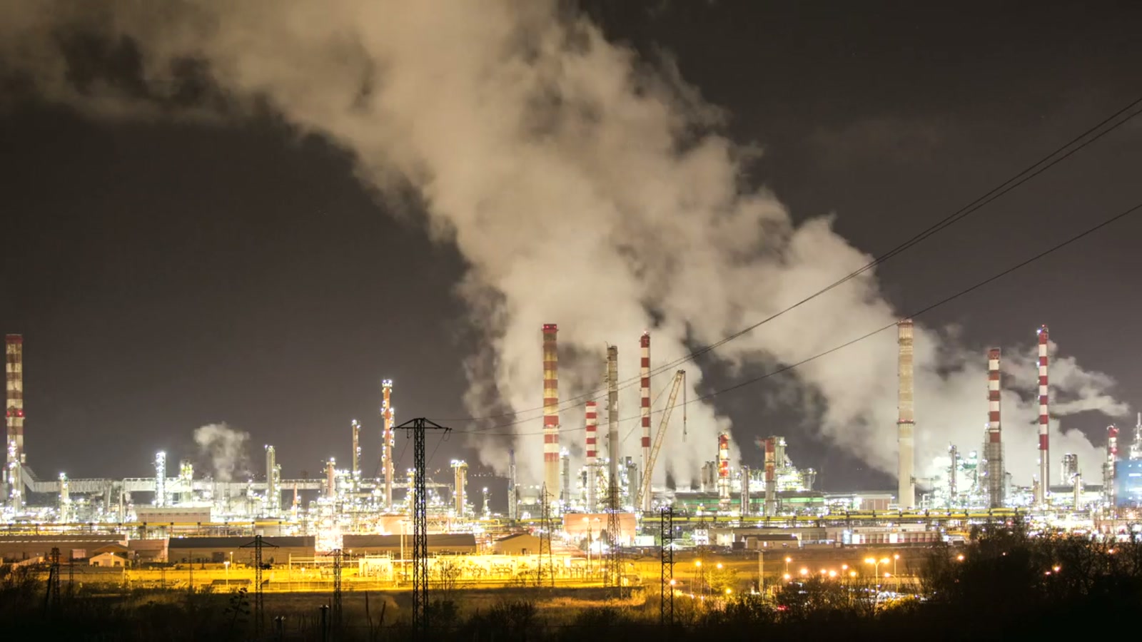 Night refinery complex with lit process units and active stack plumes.