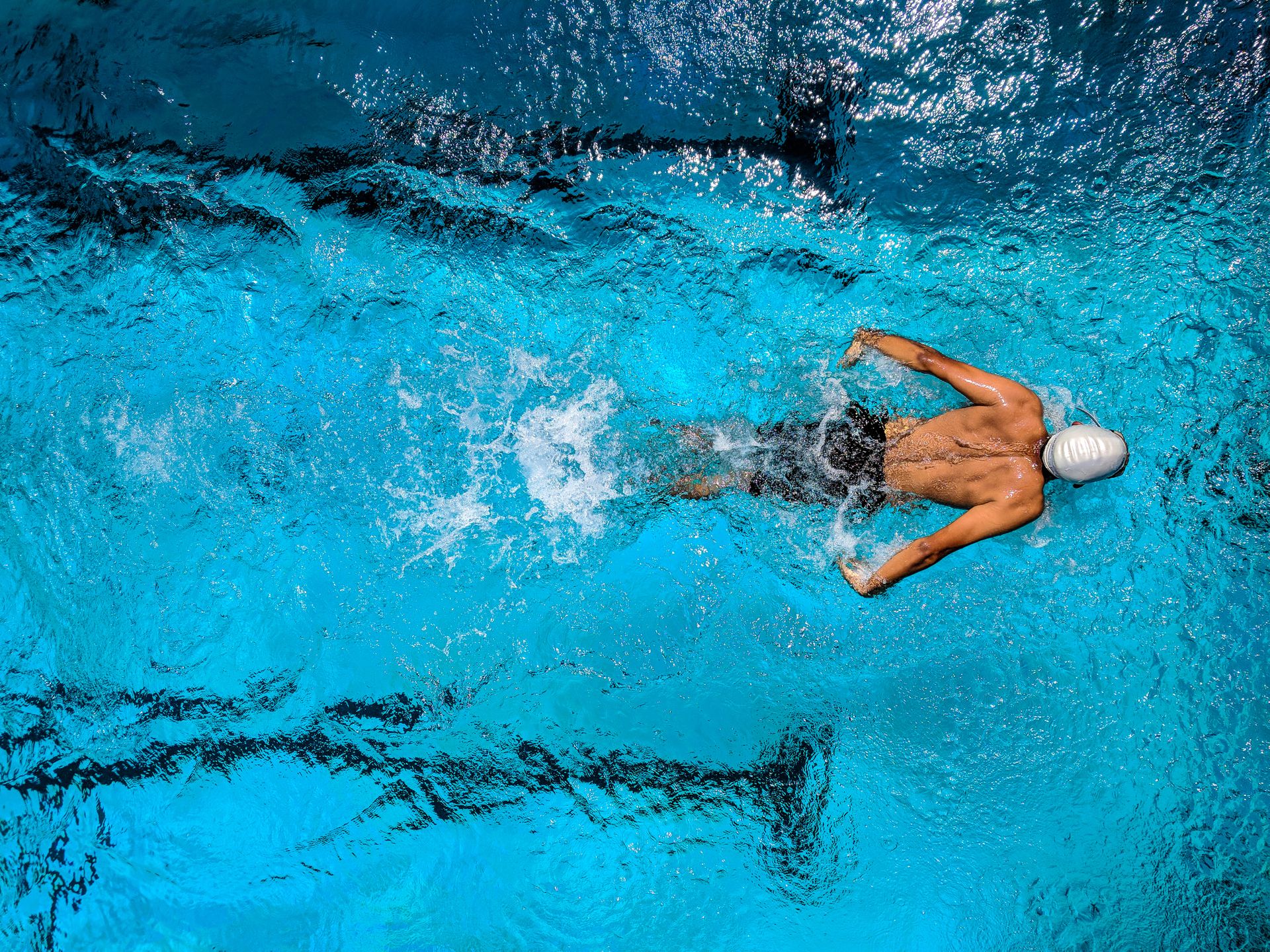 Overhead cinema still of a competitive swimmer mid-stroke, water spray and lane lines.