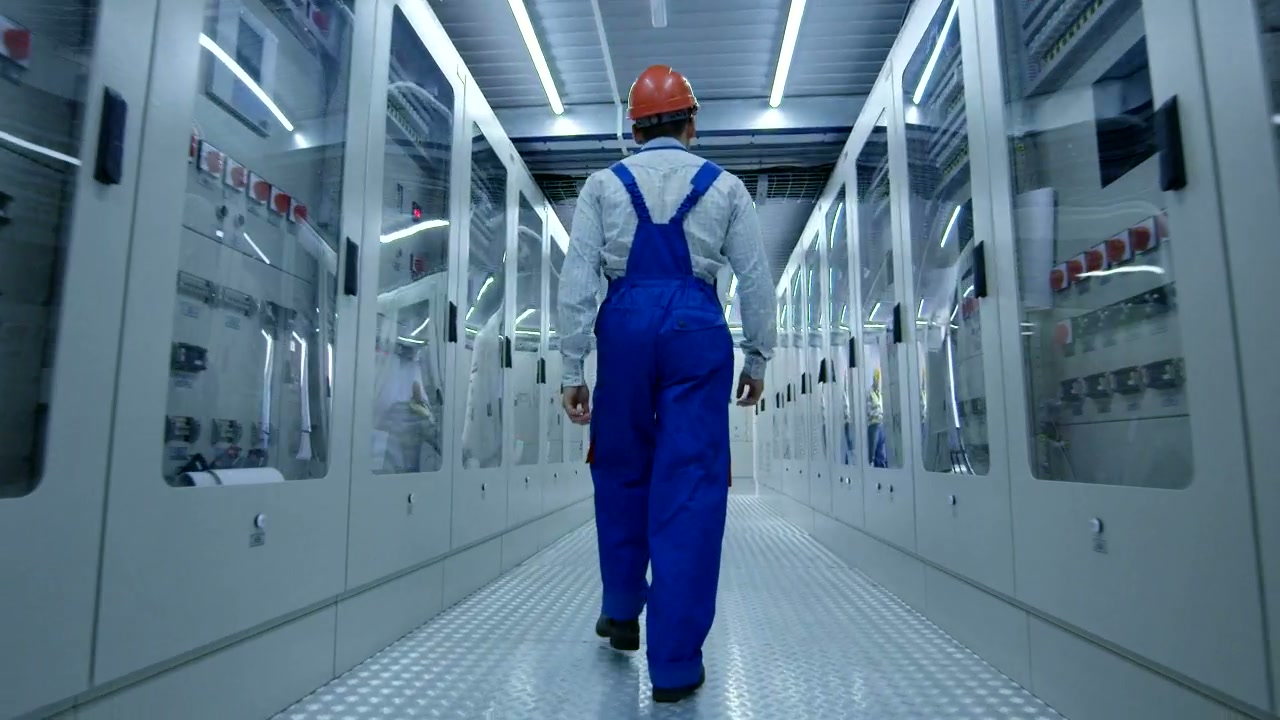 Technician walking a facility corridor lined with equipment cabinets.
