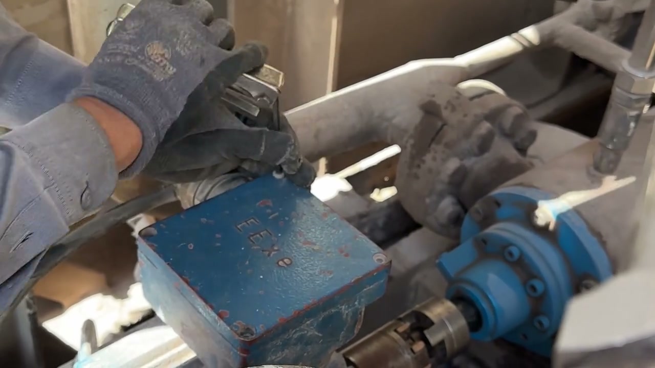 Close-up of a technician servicing a blue industrial junction box with a wrench.